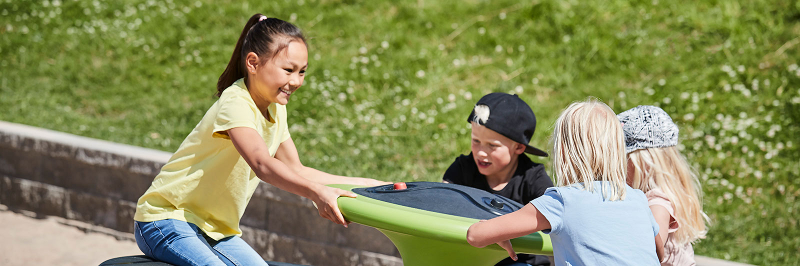 Children spin on an orbit roundabout, they are holding on and smiling.